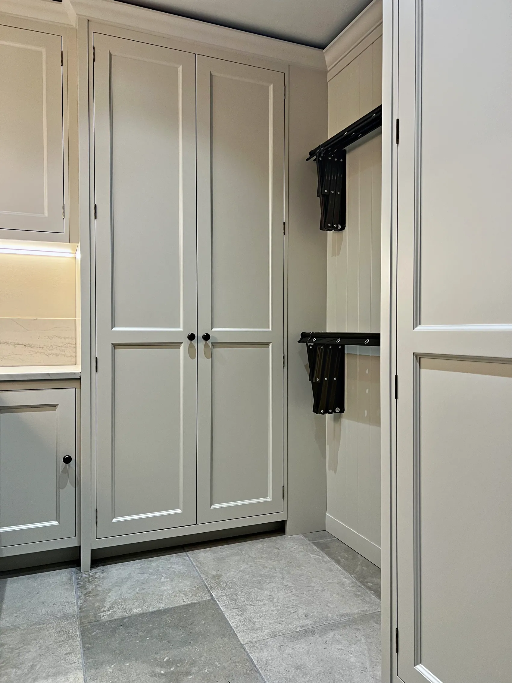 Pale grey utility with a tall double cupboard and black drying racks on a tongue and groove panel