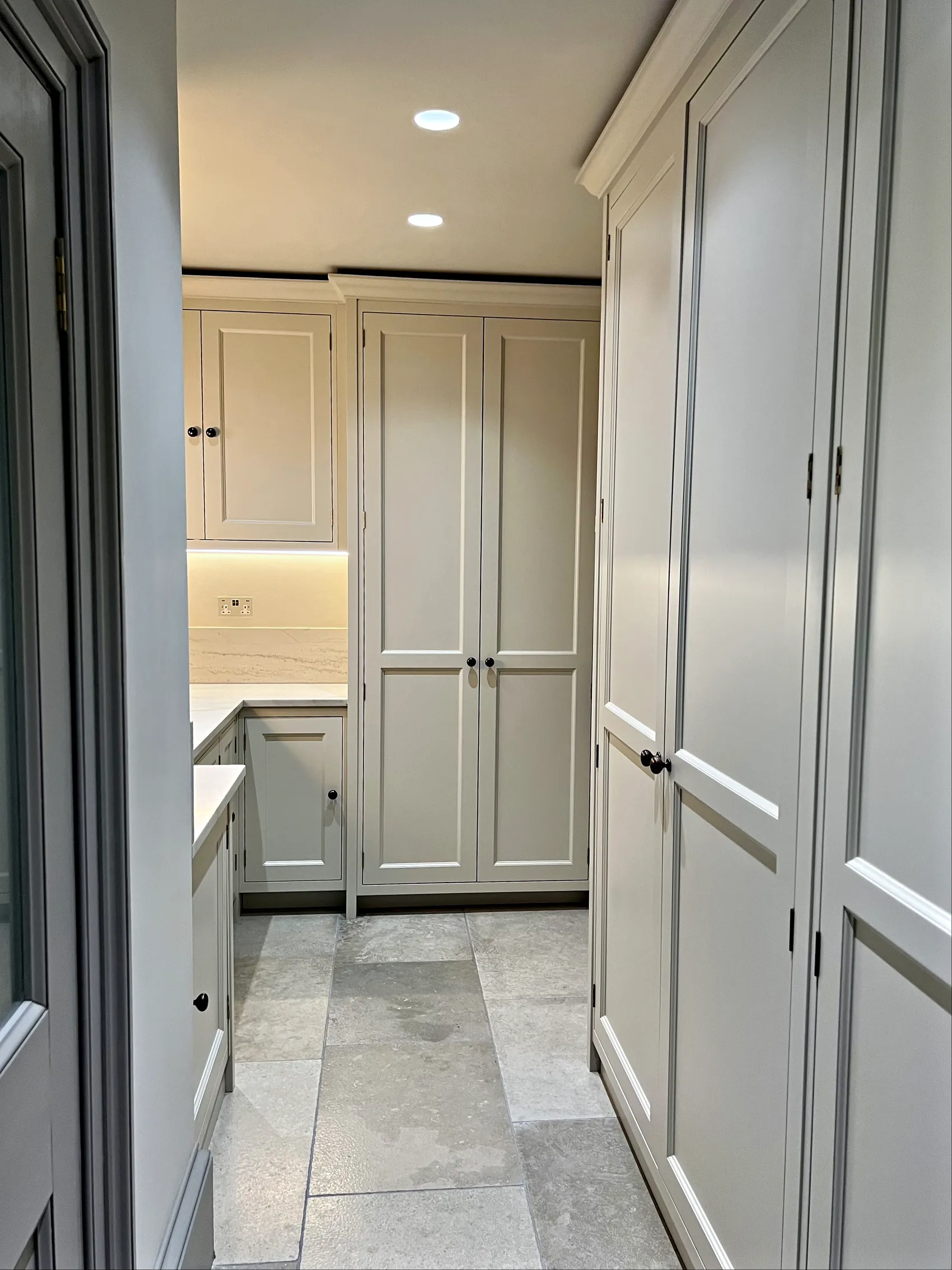 Pale grey utility passage with tall panelled cupboards, a worktop run and a grey stone floor