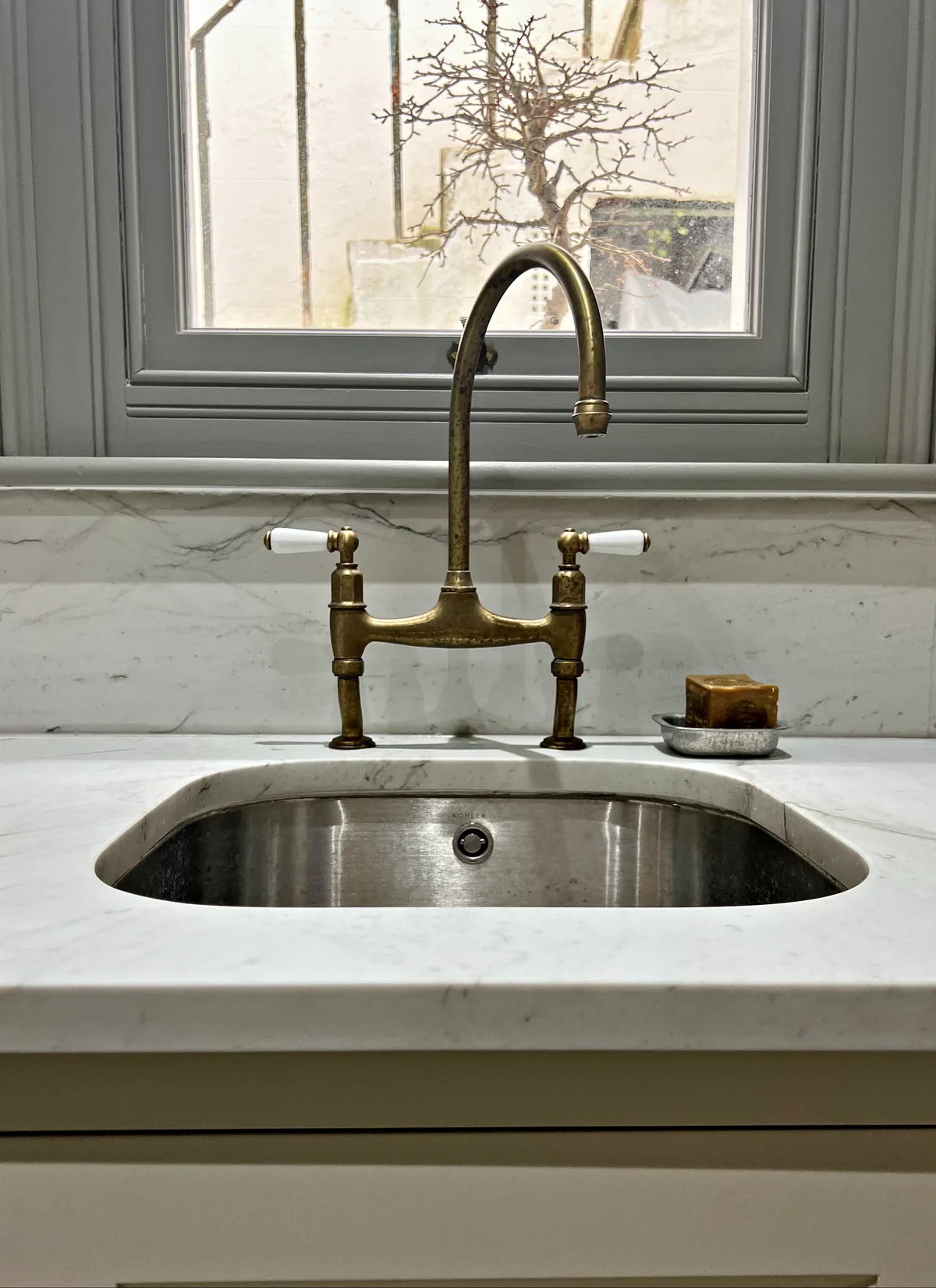 Brushed brass bridge tap over a steel undermount sink in a white veined marble top