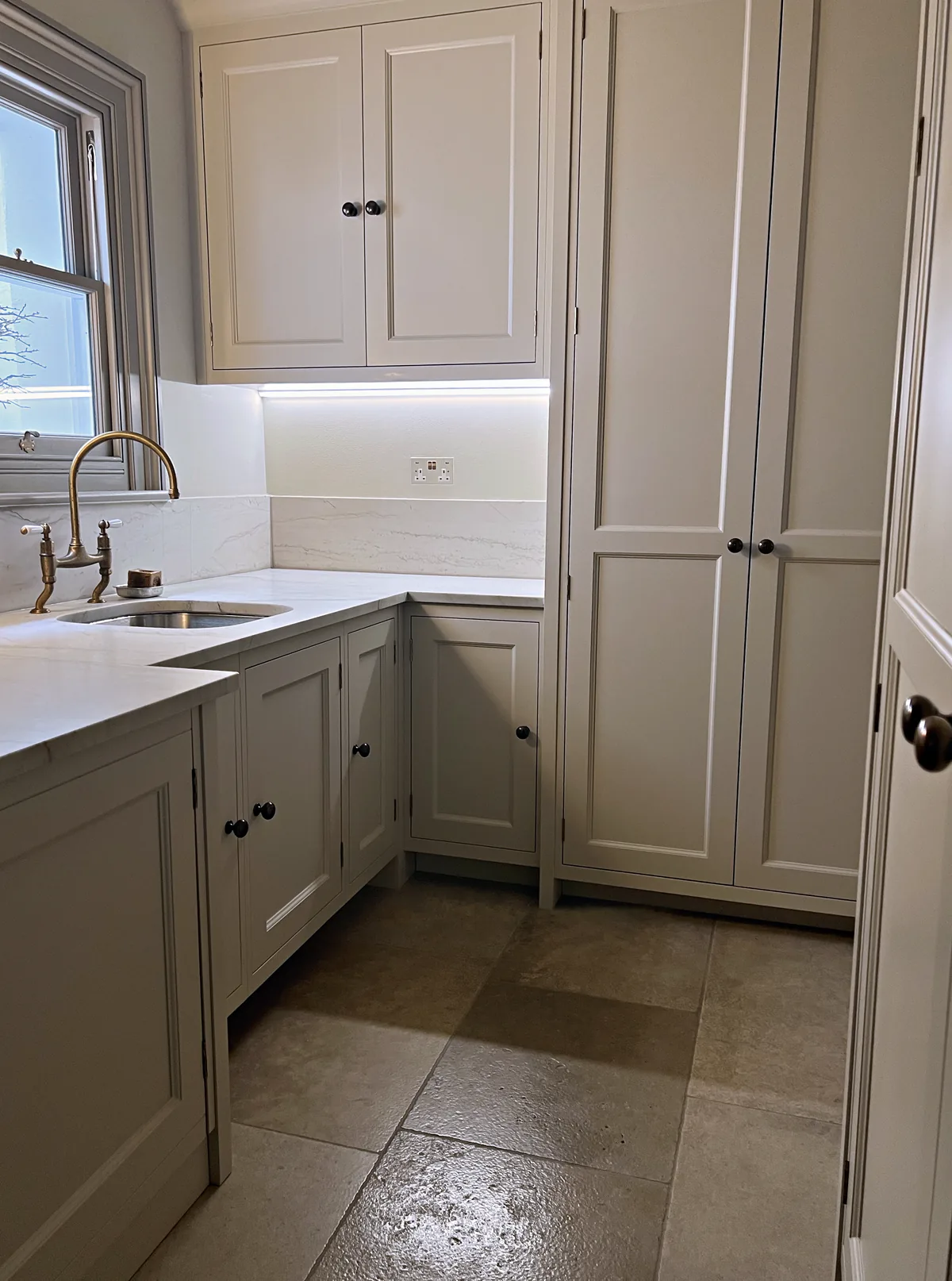 Utility with a brass bridge tap, a marble worktop and tall pale grey cupboards