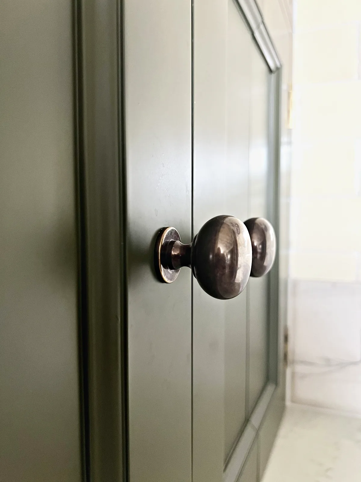 Bronze knob on an olive green painted door beside cream brick tiles