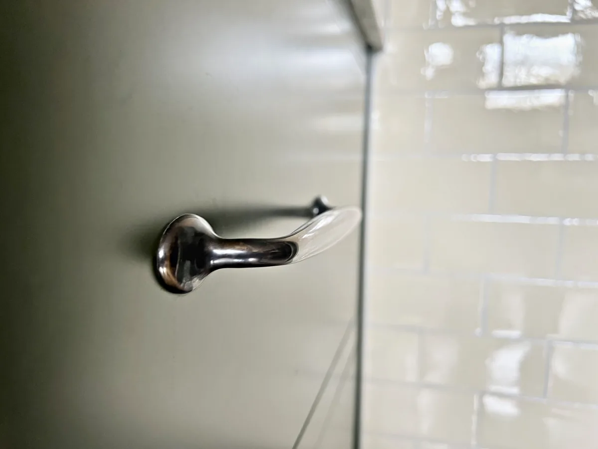 Nickel drawer pull on an olive green drawer beside cream brick tiles