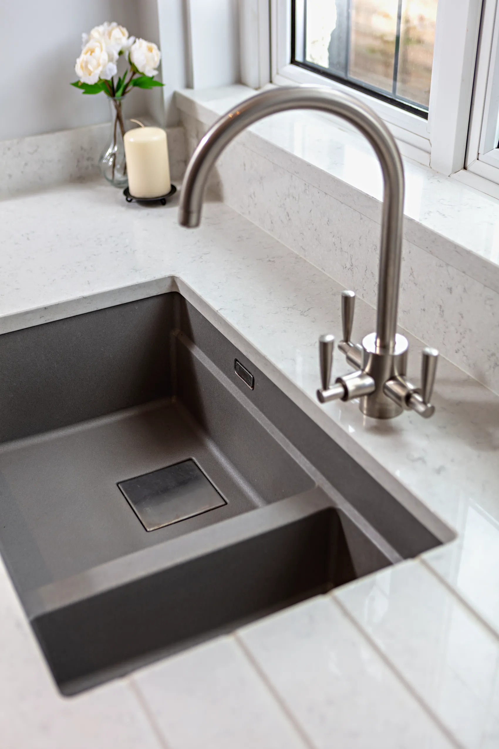 Brushed nickel tap over a dark grey composite sink with drainer grooves in a pale quartz top
