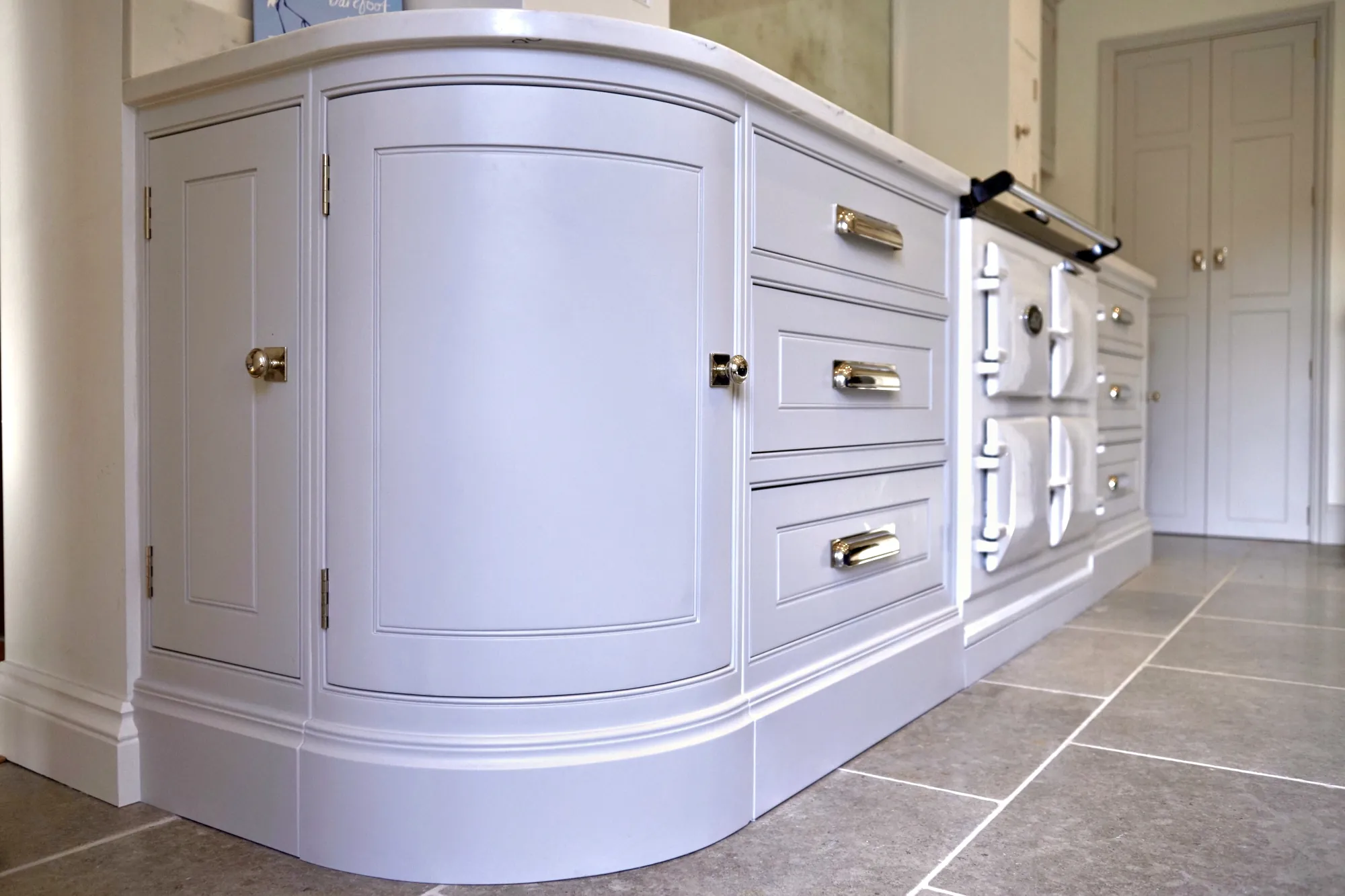 Curved end cabinet run with nickel cup handles beside a cast iron range cooker