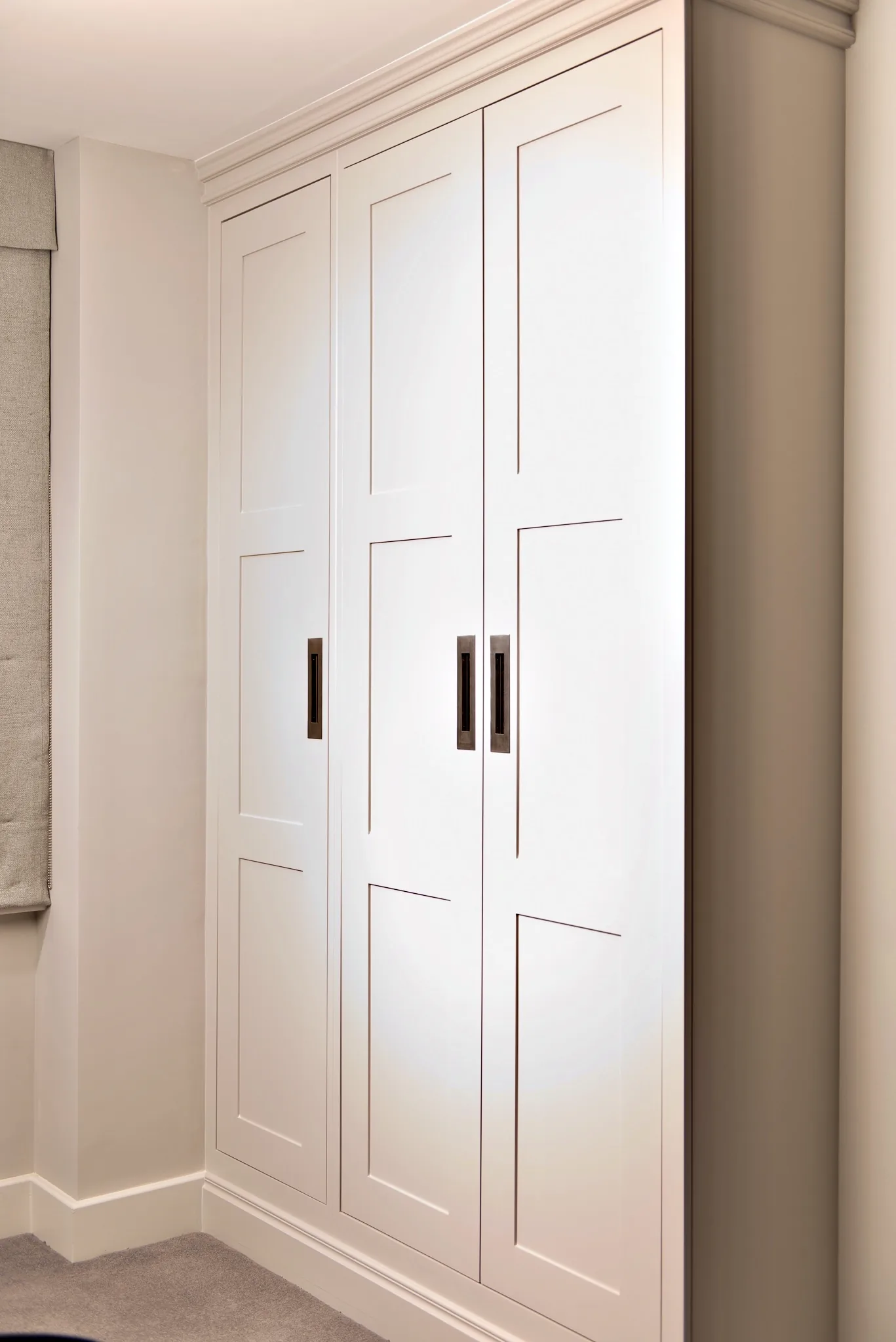 Pale painted fitted wardrobe with panelled doors and long bar handles in a bedroom