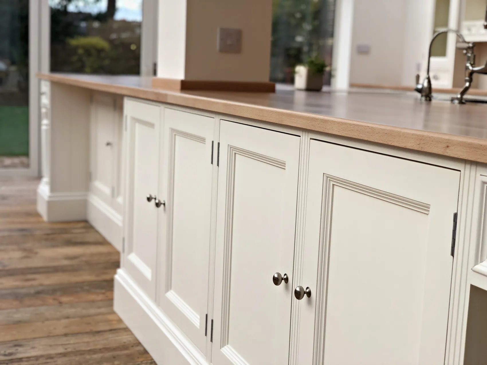 Pale painted cupboards under an oak worktop with a nickel bridge tap