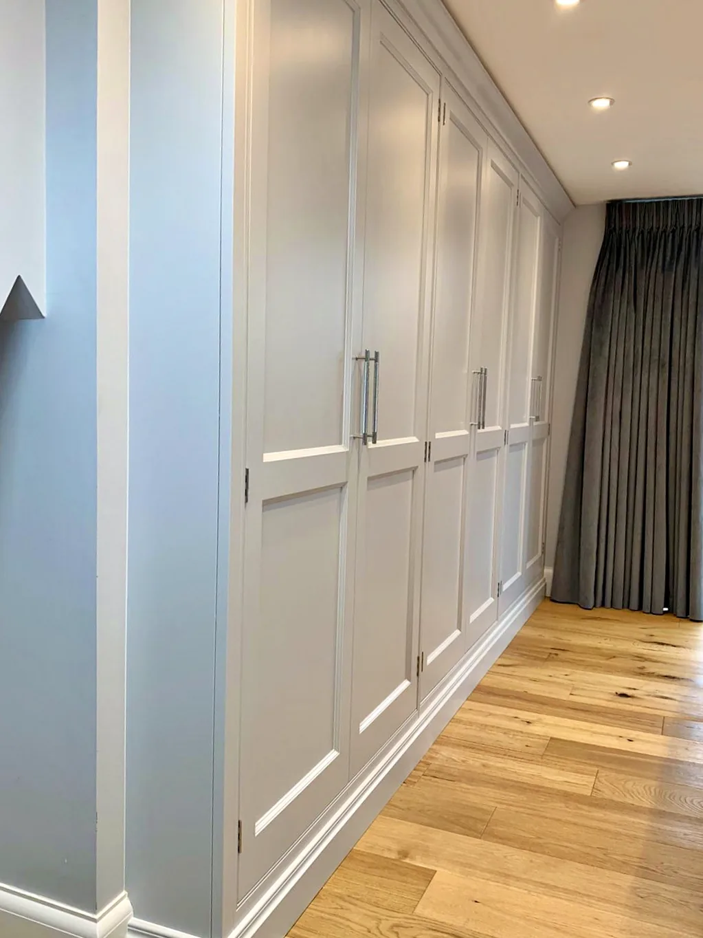 Long run of pale fitted wardrobes with bar handles on an oak floor