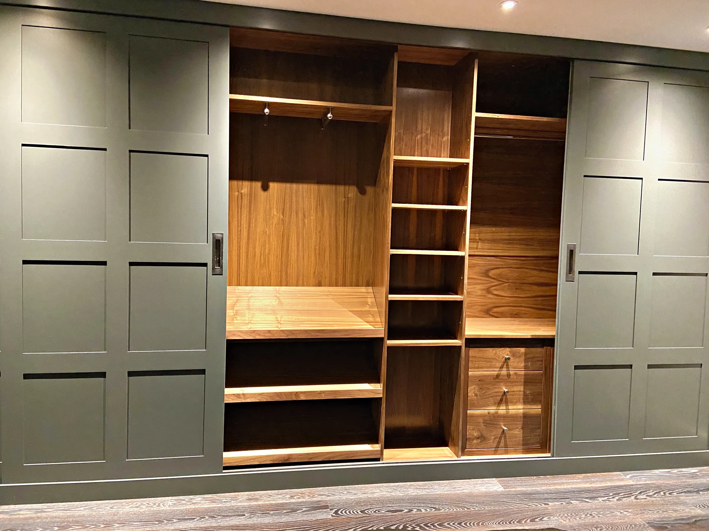 Grey green sliding wardrobe open on a walnut interior with shelves, drawers and hanging space