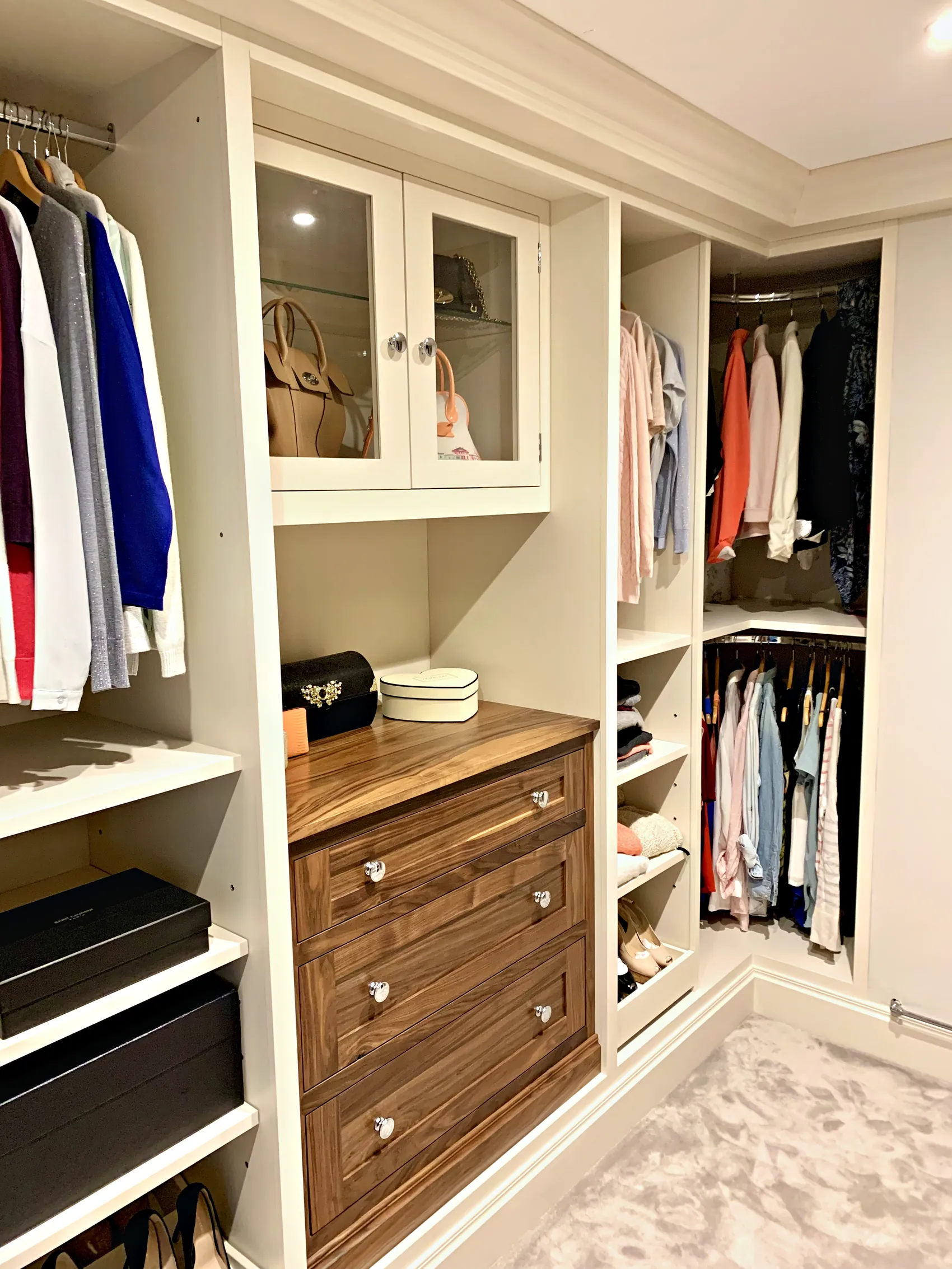 Dressing room with cream open wardrobe sections for hanging, a glazed top cupboard and walnut drawers