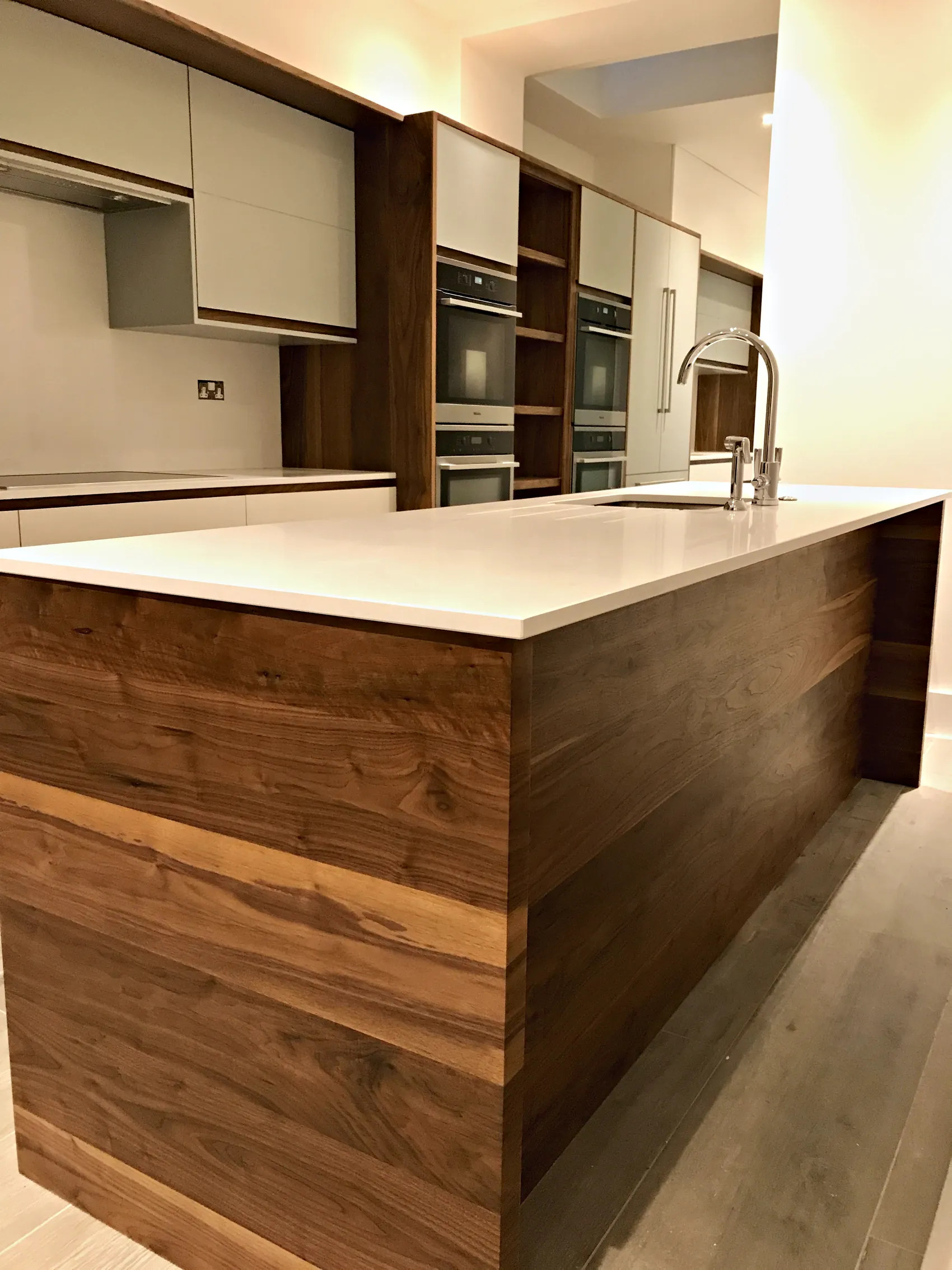Contemporary kitchen with a walnut clad island, a white worktop and grey handleless cabinetry