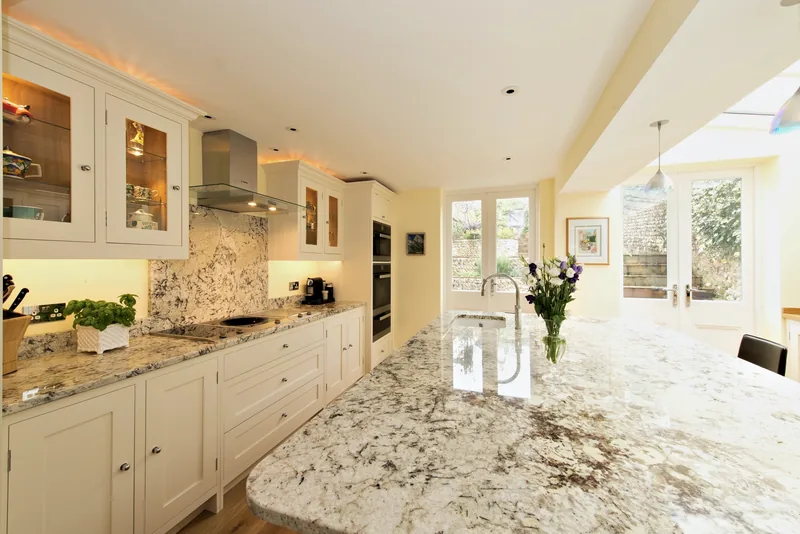 Cream kitchen with a granite topped island and lit glazed wall cabinets