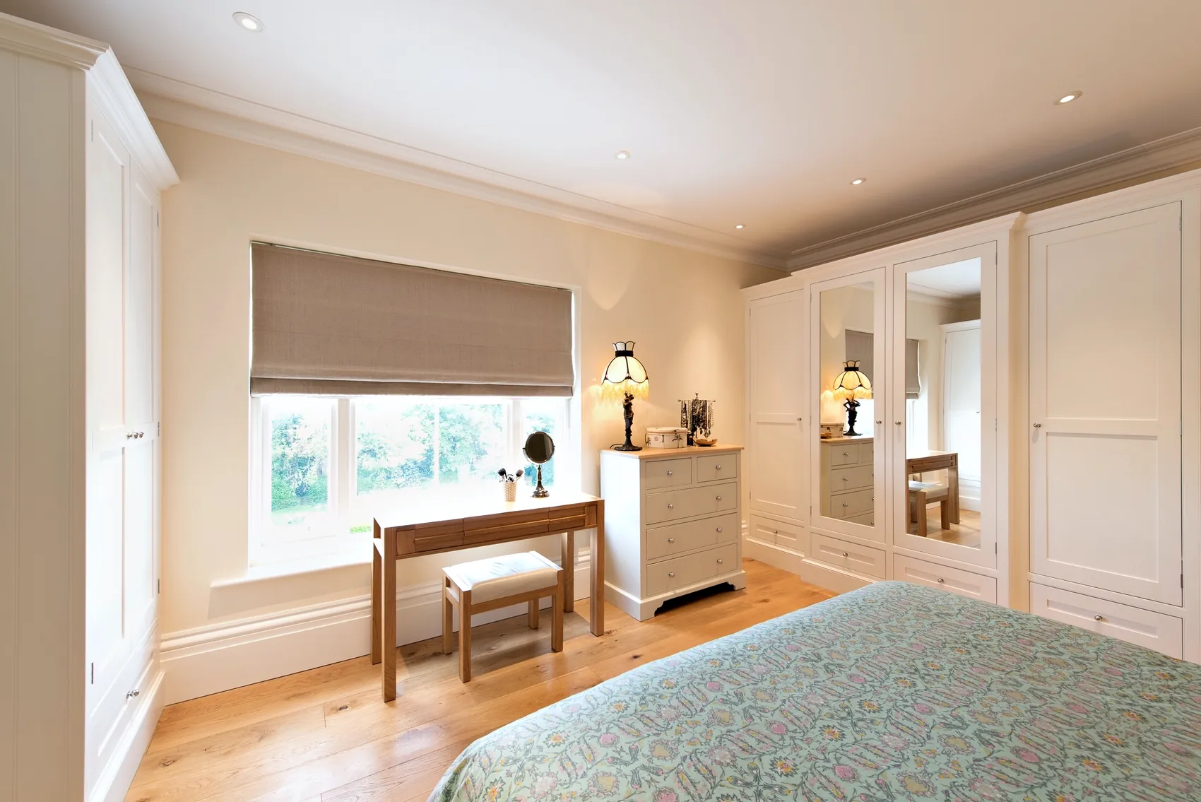 Bedroom with pale fitted wardrobes with mirrored doors, a dressing desk and a chest of drawers