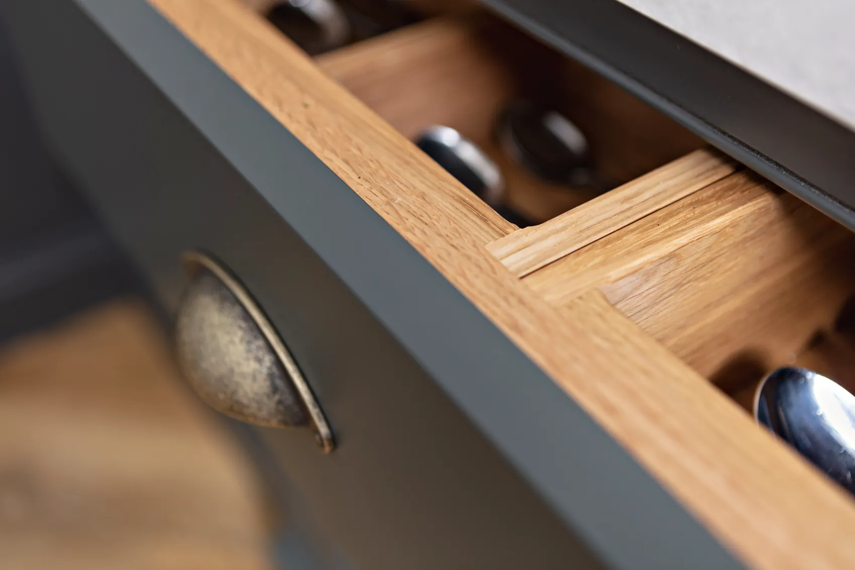 Charcoal drawer with an antique brass cup pull opened on oak dividers