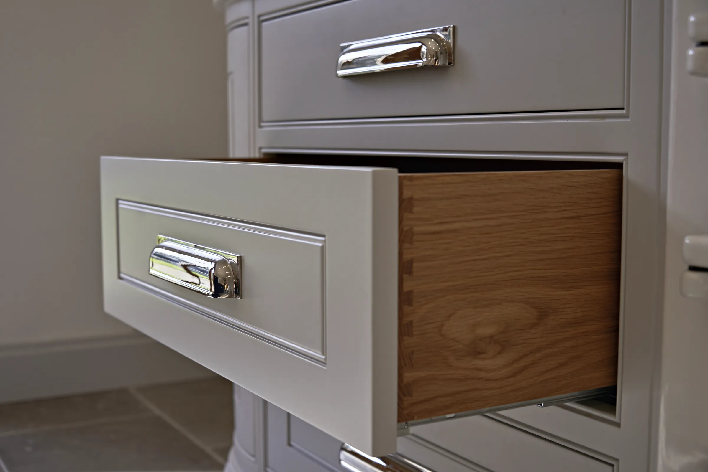 Pale grey drawer open on a dovetailed oak box with a polished chrome cup pull