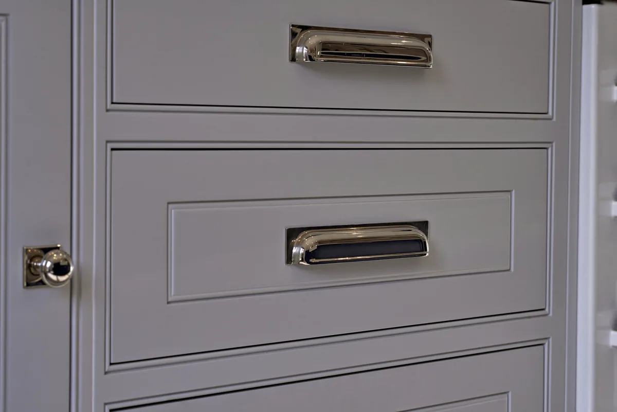 Pale grey drawers with polished chrome cup pulls and a small knob on a panelled door